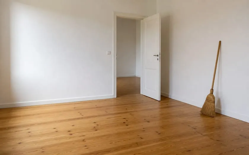 Besenreine leere Wohnung mit blankem Dielenboden und an die Wand gelehntem Besen